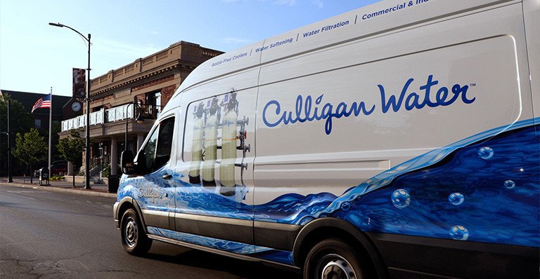 Side view of a Culligan van driving down a suburban main street